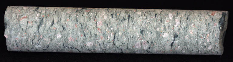 Colour image of round, tube-like sample of gray rock mottled with white and pink rock