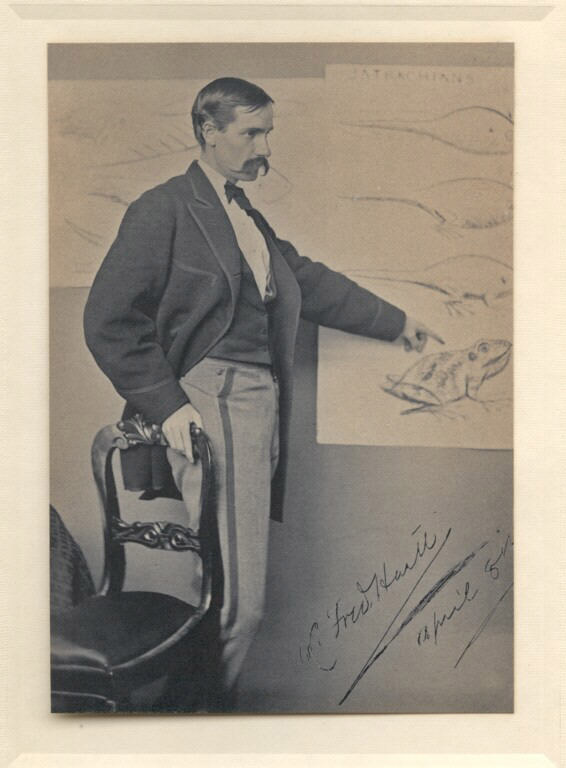 Black and white photograph of man standing and pointing at a picture on the wall